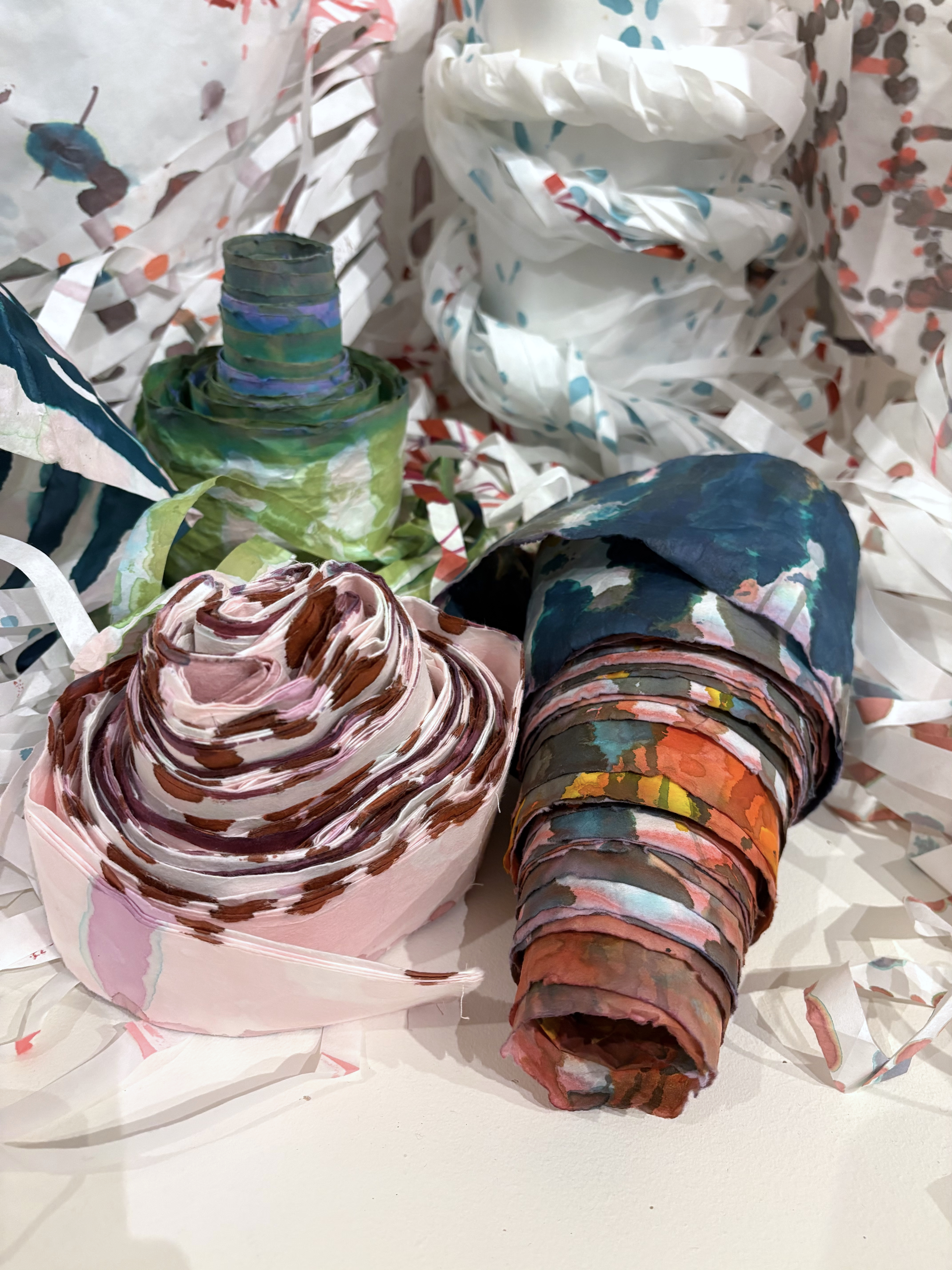 Colorfully painted paper scrolls fill the frame. They're stacked up against each other, one has toppled over. They're surrounded by fringe cut from the ends. 